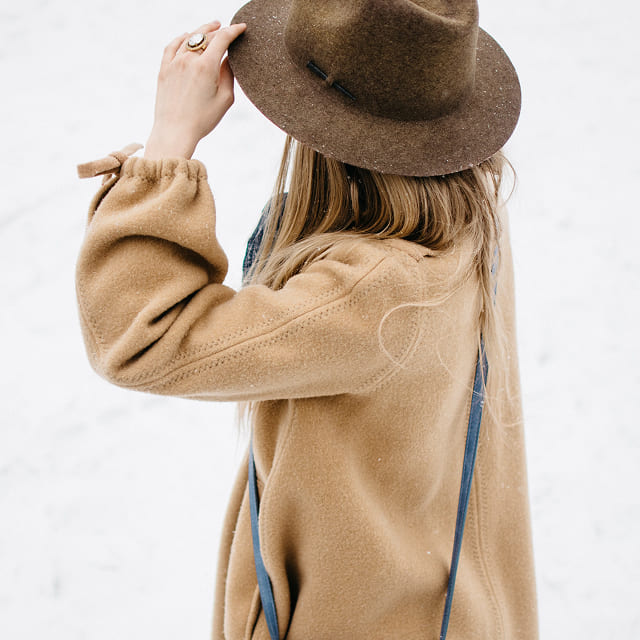 Woman styling a felt hat with a camel coat